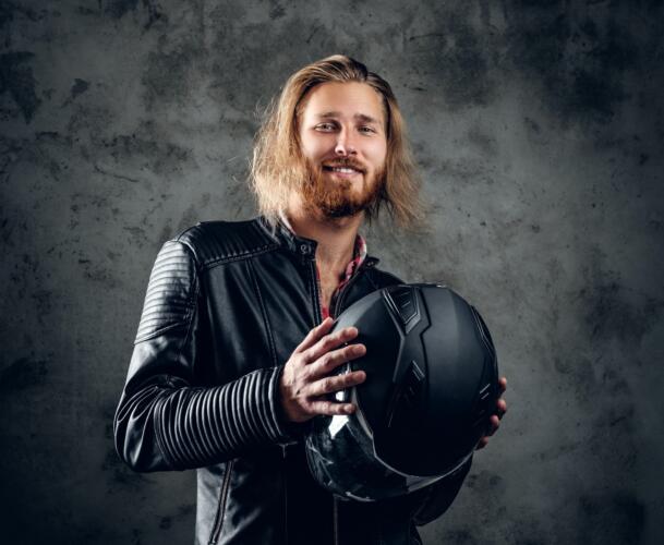 A man in leather jacket holds motorcycle helmet.