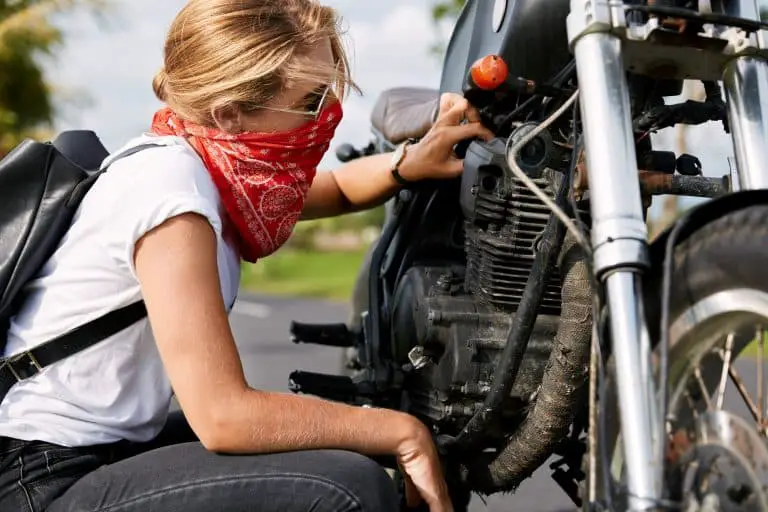 Professional young female biker in casual clothing, wears bandana covedred face, tries to solve mech