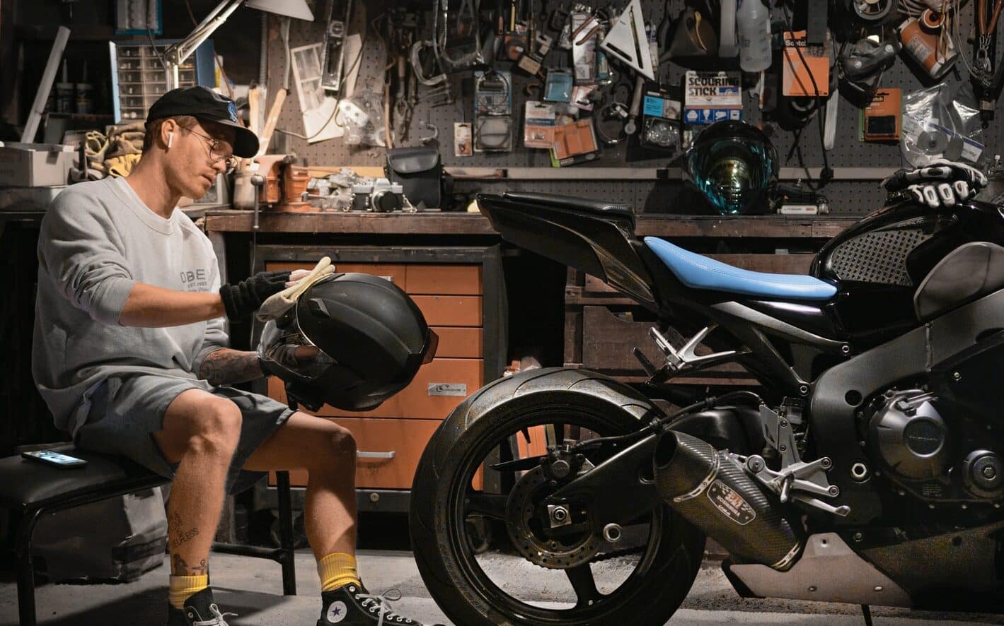 man wiping motorcycle helmet by motorcycle