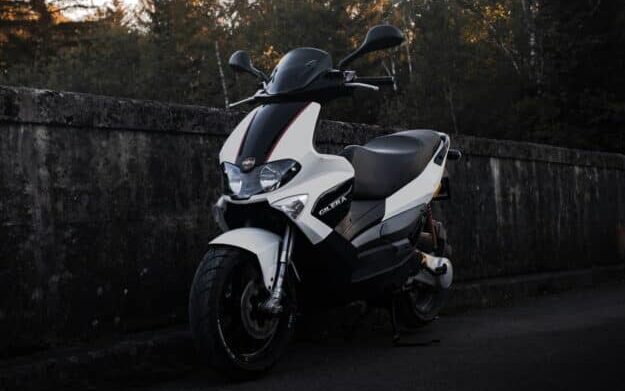 white and black motor scooter parked beside gray concrete wall during daytime